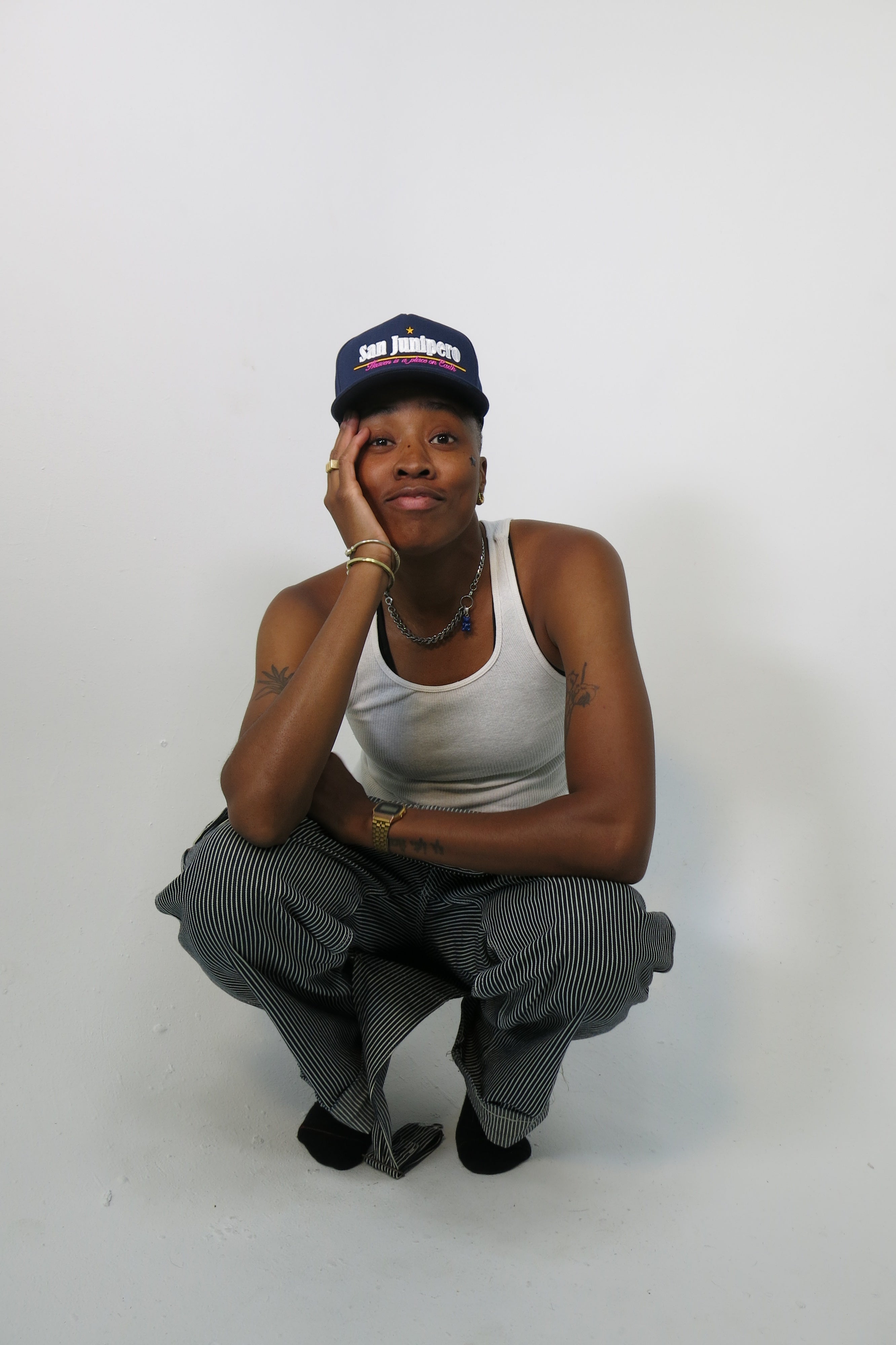 Mal Wright crouches wearing a San Junipero hat, designed in collaboration with For Them